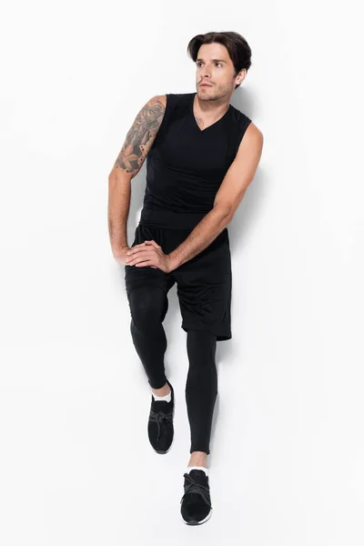 Longitud completa del hombre tatuado en ropa deportiva de pie sobre fondo gris - foto de stock