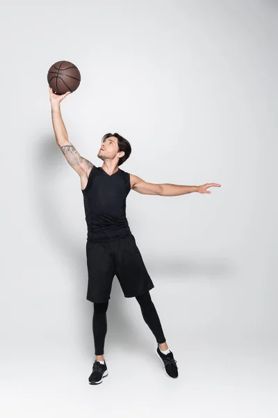 Спортсмен, що піднімається баскетбольний м'яч на сірому фоні — стокове фото