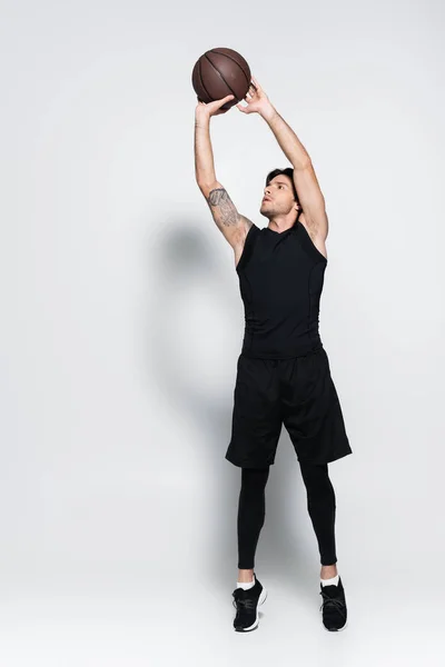 Full length of sportsman throwing basketball ball while training on grey background — Stockfoto