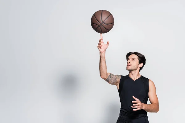 Deportista tatuado sosteniendo pelota de baloncesto en el dedo sobre fondo gris - foto de stock