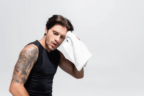 Уставший спортсмен вытирает лицо полотенцем, изолированным на сером — стоковое фото