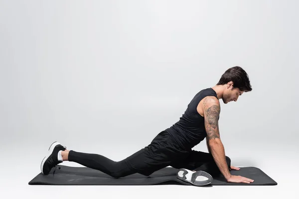 Side view of sportsman stretching leg on fitness mat on grey background — Stock Photo