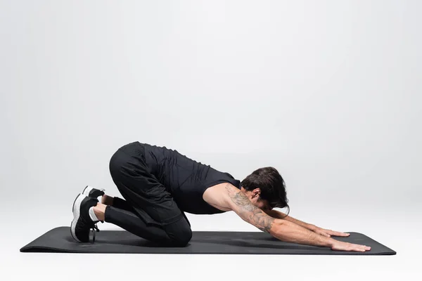 Morena deportista estiramiento en la alfombra de fitness sobre fondo gris - foto de stock