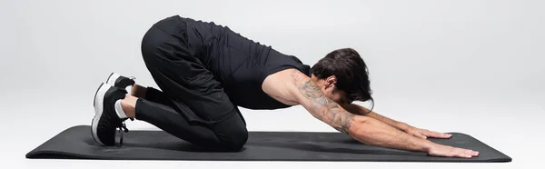 Deportista tatuado estirándose en la alfombra de fitness sobre fondo gris, pancarta - foto de stock