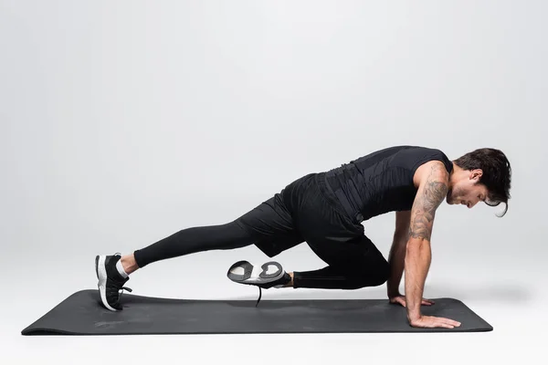 Side view of sportsman working out on black fitness mat on grey background — Stock Photo