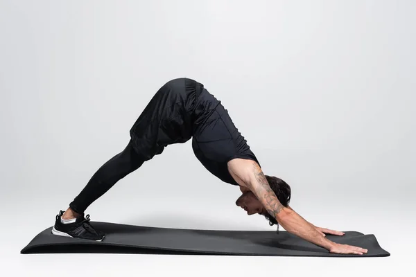 Vue latérale du sportif qui se penche en s'étirant sur un tapis de fitness sur fond gris — Photo de stock