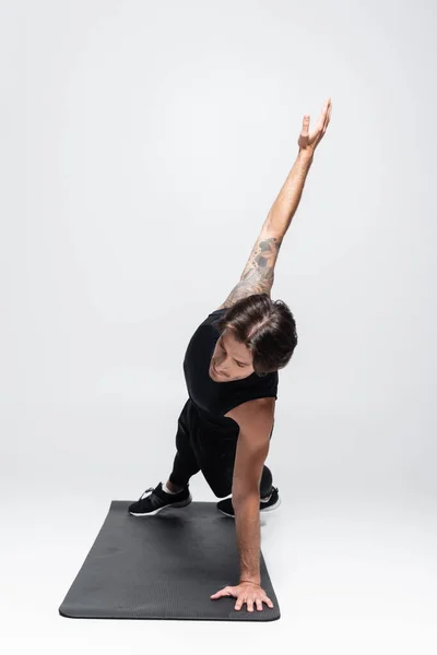 Sportif tatoué faisant planche latérale sur tapis de fitness sur fond gris — Photo de stock