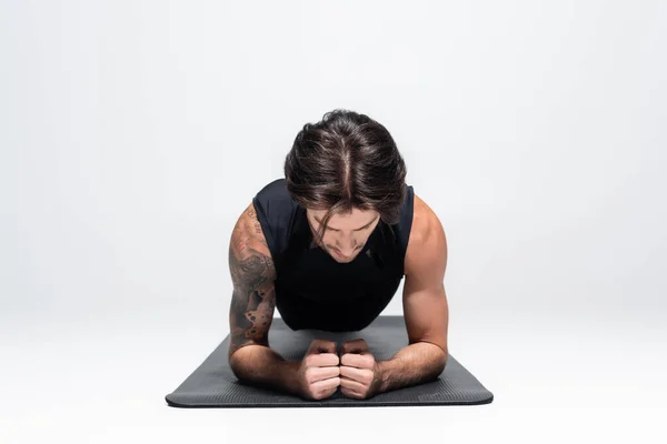 Sportsman in sleeveless shirt doing plank on fitness mat on grey background — Stockfoto