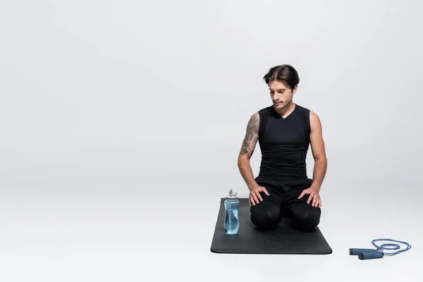 Deportista mirando la botella de deportes cerca de saltar la cuerda sobre fondo gris - foto de stock