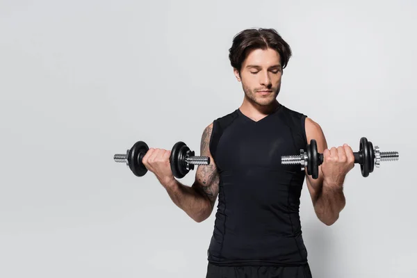 Brunette sportsman looking at dumbbells on grey background — Stockfoto