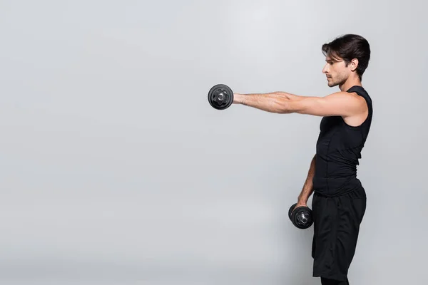 Vista lateral del entrenamiento deportivo con mancuernas aisladas en gris — Stock Photo