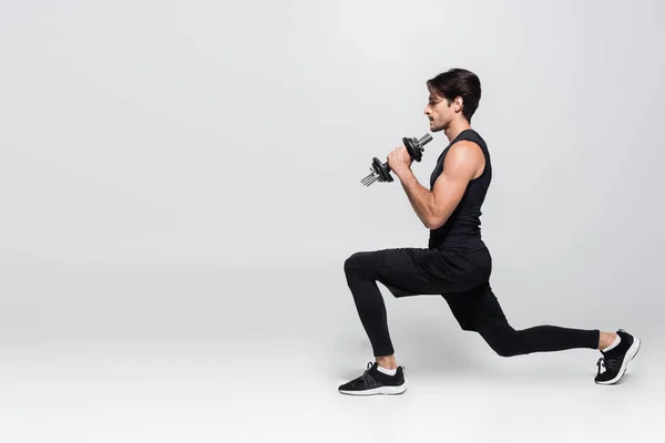 Side view of sportsman doing lunges and holding dumbbells on grey background — Stock Photo