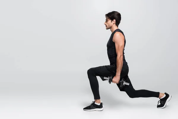 Side view of fit man training with dumbbell on grey background — Stock Photo