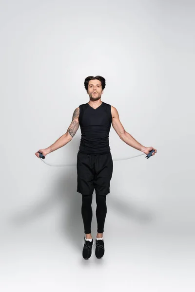 Татуйований спортсмен тренування зі стрибковою мотузкою на сірому фоні — стокове фото