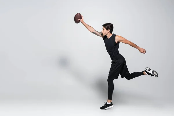 Side view of player with rugby ball running on grey background — Foto stock