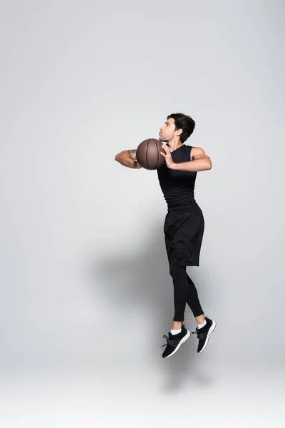 Side view of basketball player with ball jumping on grey background — Foto stock