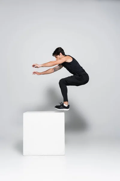 Sportler springt auf weißem Würfel auf grauem Hintergrund — Stockfoto