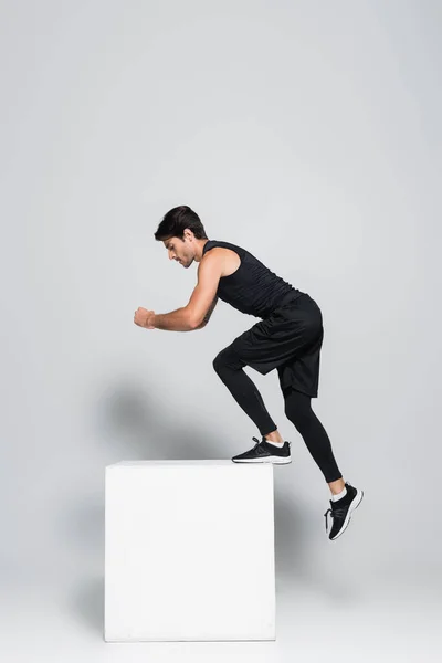 Vista lateral del deportista en ropa deportiva negra haciendo ejercicio con cubo sobre fondo gris - foto de stock