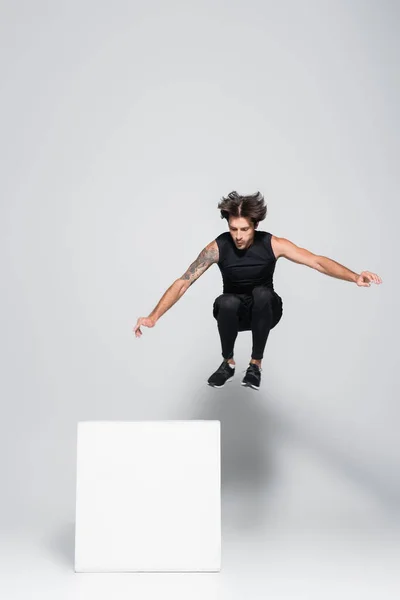Спортсмен стрибає біля кубика на сірому фоні — стокове фото
