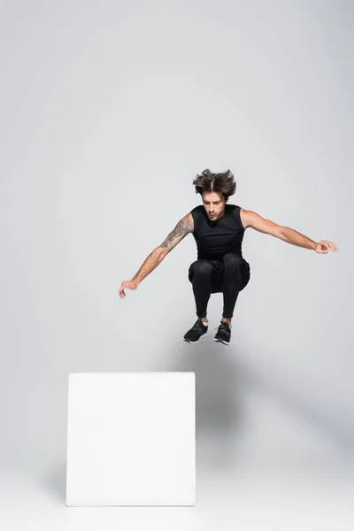 Sportsman jumping near cube on grey background — Stock Photo