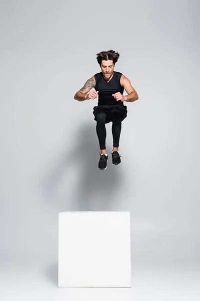 Athletic sportsman jumping above cube on grey background — Stockfoto