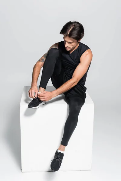 Tätowierter Sportler bindet Schnürsenkel auf Würfel auf grauem Hintergrund — Stockfoto
