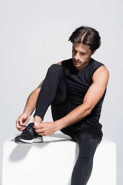 Brunette sportsman tying shoelaces on cube isolated on grey — Stock Photo