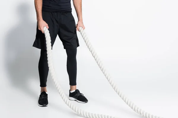 Cropped view of sportsman holding battle ropes on grey background — Stock Photo