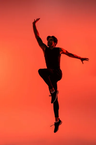 Athletic sportsman in black sportswear jumping on red background — Stock Photo