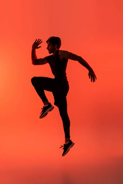 Side view of sportsman jumping on red background — Foto stock