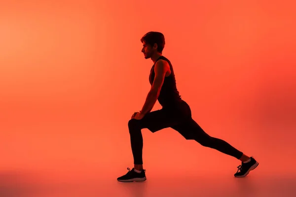 Side view of athletic sportsman training on red background — Foto stock