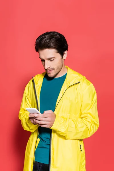 Sportsman in sports jacket using smartphone on red background — Stock Photo