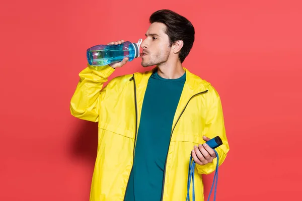 Brunette sportsman holding skipping rope and drinking water on red background — Foto stock