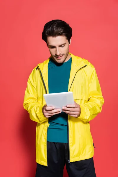 Esportista em casaco esportivo amarelo usando tablet digital em fundo vermelho — Fotografia de Stock