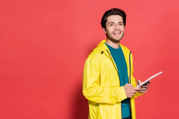 Sportler hält digitales Tablet in der Hand und lächelt in die Kamera auf rotem Hintergrund — Stockfoto