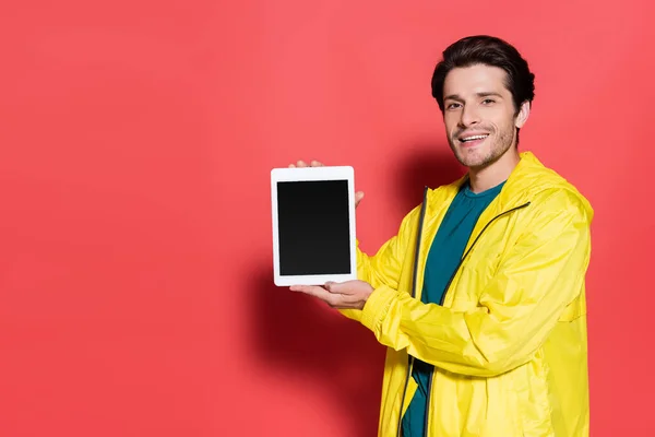 Esportista positivo segurando tablet digital com tela em branco no fundo vermelho — Fotografia de Stock