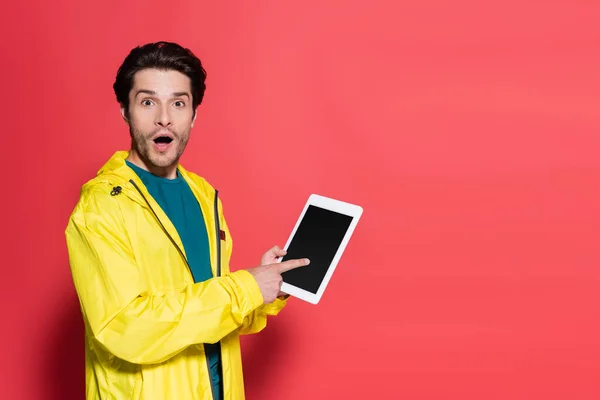 Sportif excité pointant vers la tablette numérique avec écran blanc sur fond rouge — Photo de stock