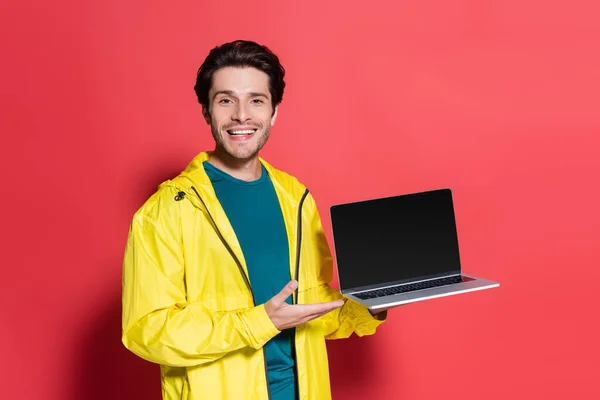 Lächelnder Sportler zeigt auf Laptop mit leerem Bildschirm auf rotem Hintergrund — Stockfoto