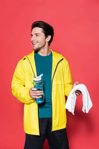 Deportista feliz sosteniendo la toalla y la botella de deportes sobre fondo rojo - foto de stock