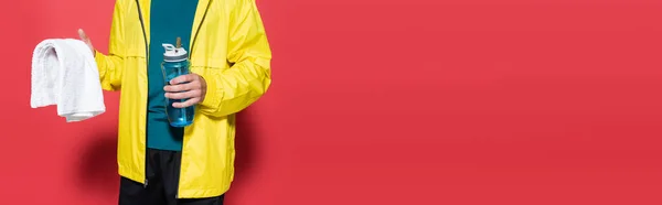 Cropped view of sportsman holding sports bottle and towel on red background, banner — Foto stock