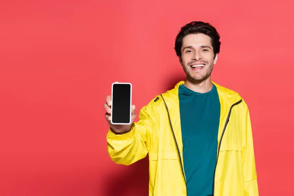 Desportista morena mostrando smartphone com tela em branco no fundo vermelho — Fotografia de Stock