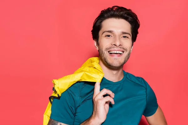 Deportista sonriente sosteniendo chaqueta deportiva amarilla y mirando a la cámara sobre fondo rojo - foto de stock