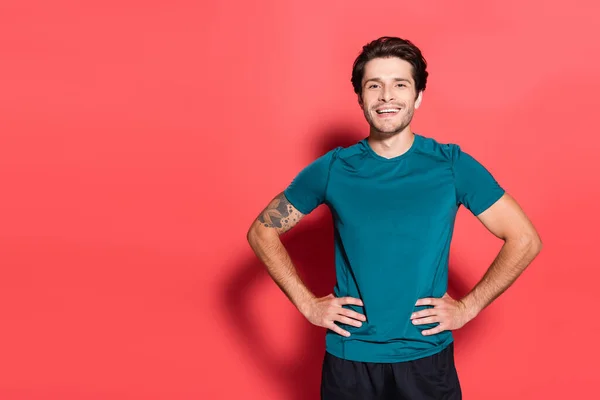 Deportista sonriente cogido de la mano en las caderas sobre fondo rojo - foto de stock