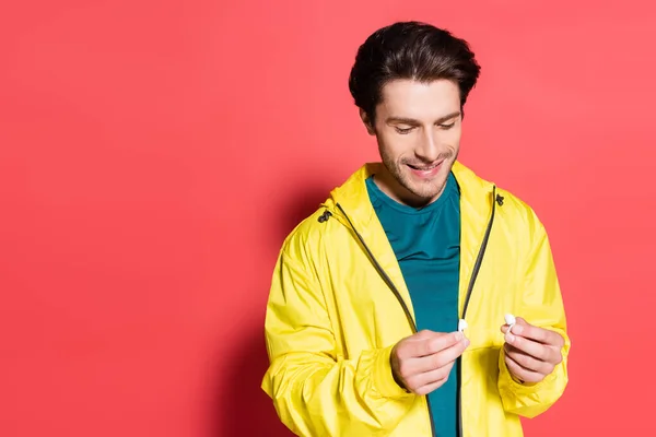 Alegre deportista sosteniendo auriculares inalámbricos sobre fondo rojo - foto de stock