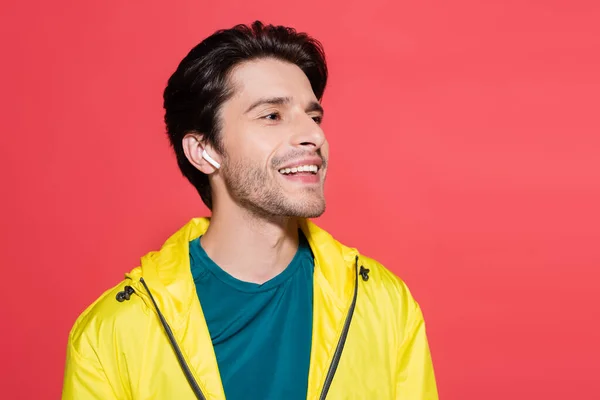 Morena desportista em fone de ouvido sem fio sorrindo isolado no vermelho — Fotografia de Stock