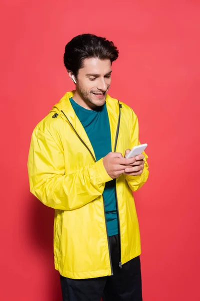 Desportista feliz no fone de ouvido usando celular no fundo vermelho — Fotografia de Stock