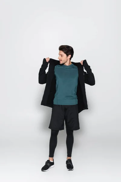 Toute la longueur du sportif portant une veste de sport sur fond gris — Photo de stock