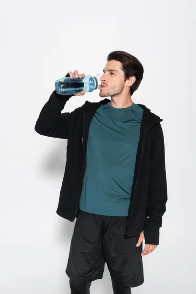 Sportsman in sports jacket drinking water on grey background — Stock Photo