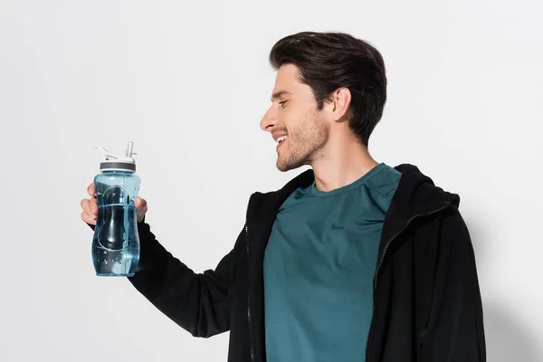 Side view of smiling sportsman looking at sports bottle on grey background — Stock Photo