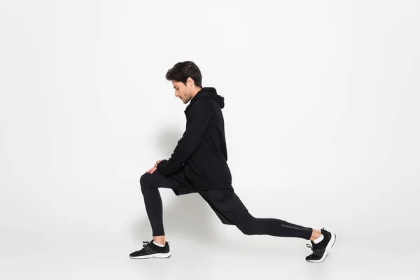 Side view of sportsman in sports jacket doing lunges on grey background — Stock Photo